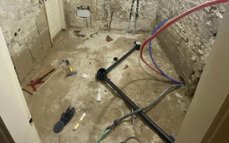 חדר רחצה בשיפוץ: צנרת מים חדשה באדום ובכחול וצנרת ניקוז שחורה על הרצפה